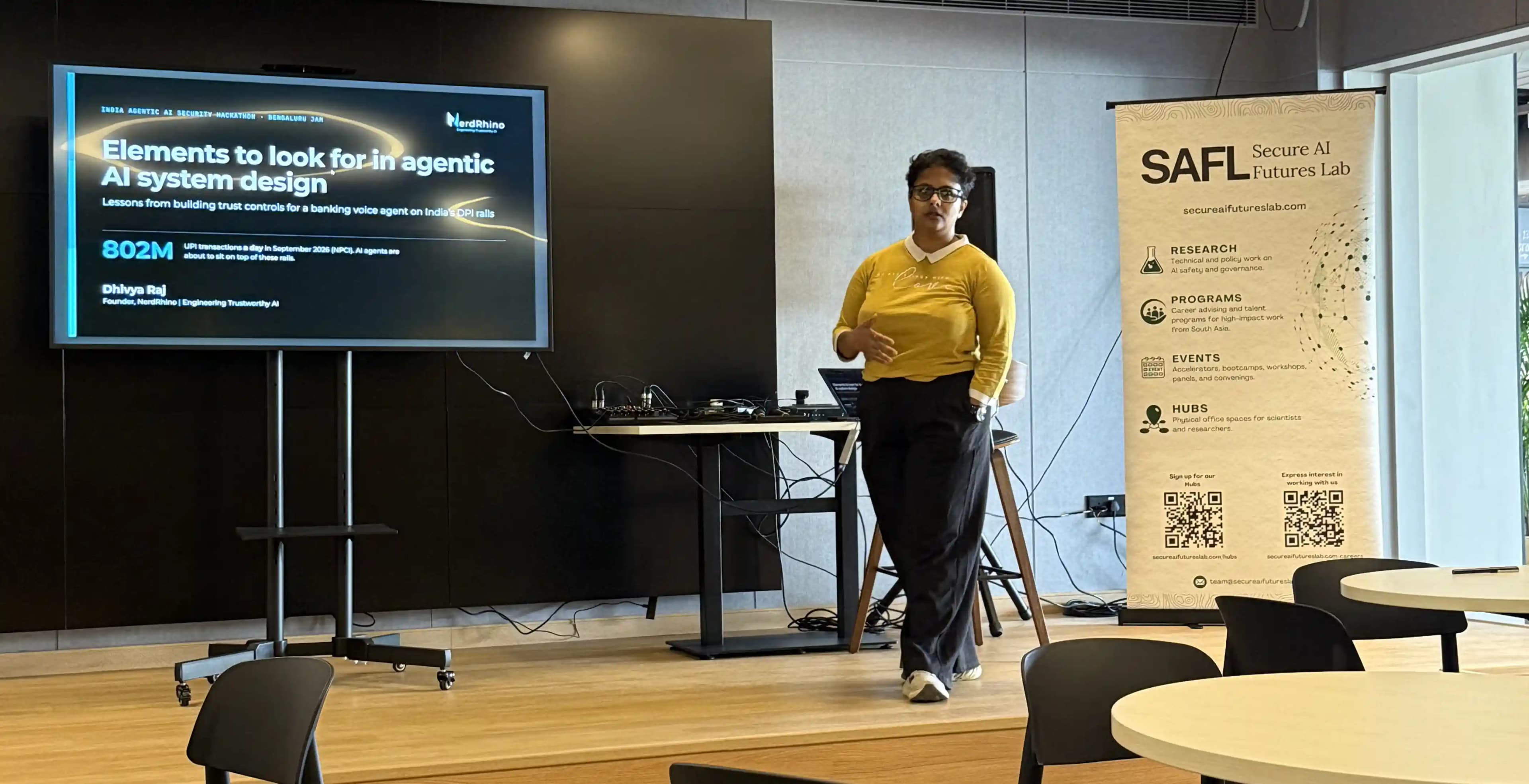 A speaker presenting on elements to look for in agentic AI system design, beside a SAFL banner